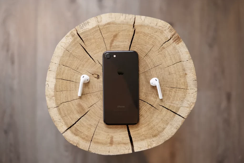 Airpods, primeiro e principal Weareable da Apple, ao lado de um Iphone sobre um banco de madeira