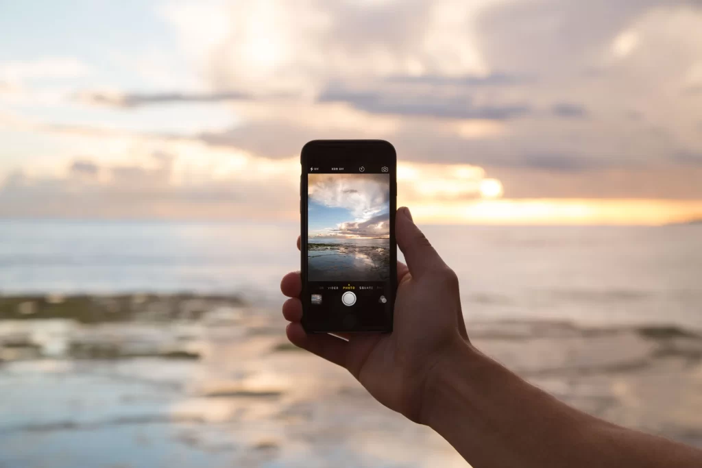 Iphone, principal produto em vendas da Apple, sendo segurado em uma praia, demonstrando a capacidade da sua câmera